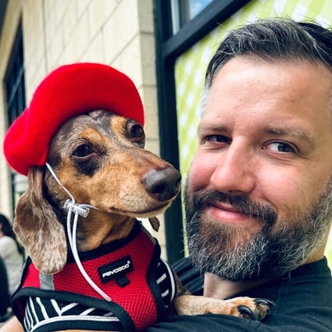 Ken Erwin holding his dachshund, who is wearing a red beret